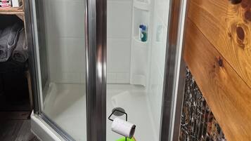A glass-enclosed shower with a wooden wall, a towel rack, and a shelf with toiletries.
