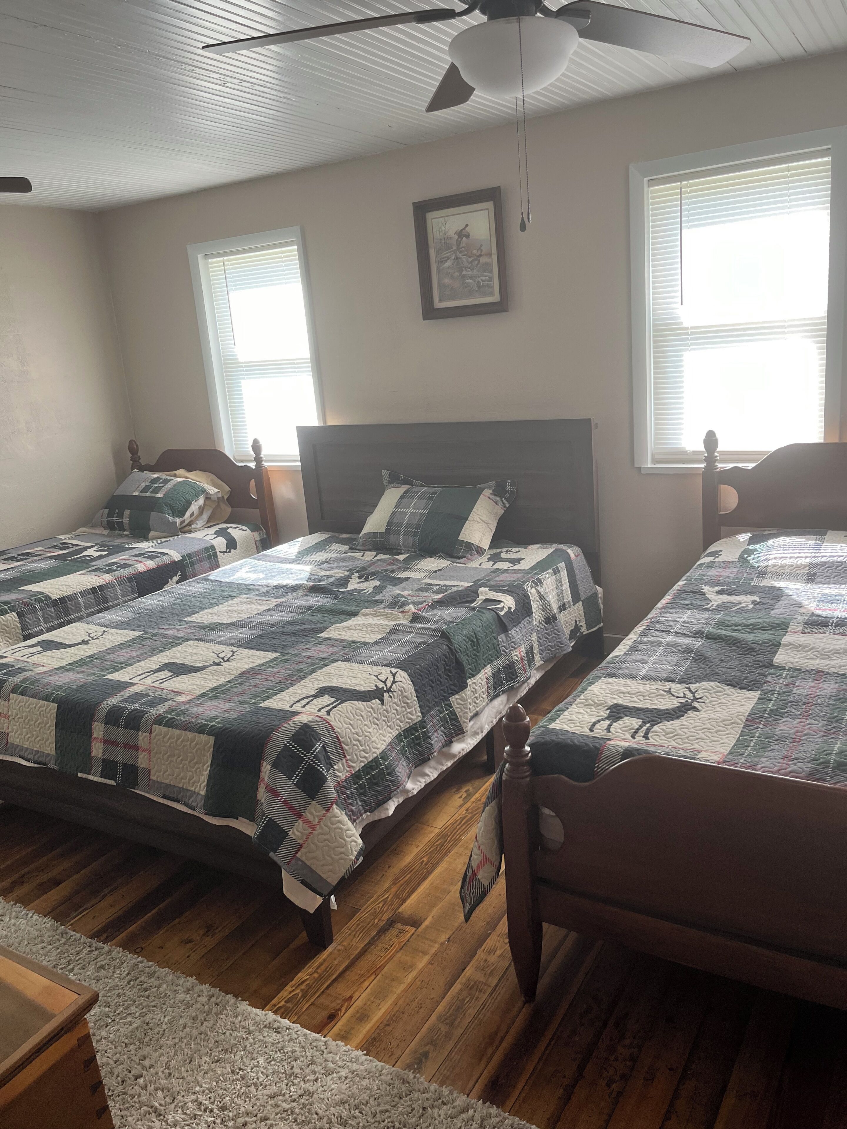 Une chambre avec deux lits, des têtes de lit en bois, un ventilateur de plafond et une fenêtre avec des stores.