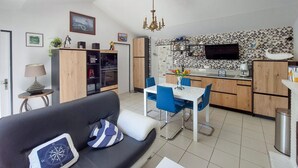 Ein modernes Wohnzimmer mit einer schwarzen Couch, einem Esstisch mit blauen Stühlen und einer Küchenzeile mit Fliesenrückwand und Holzschränken.