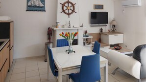 Ein modernes Wohnzimmer mit Esstisch, blauen Stühlen, einer Couch, einem Fernseher und Dekorationselementen, darunter ein Schiffsschwengel und ein Segelbootgemälde.