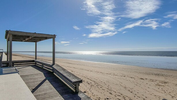 Ein Strand mit einer Holzterrasse und einer Metallpergola.