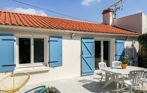 A house with a tiled roof, blue shutters, a white exterior, and a patio with a table and chairs.