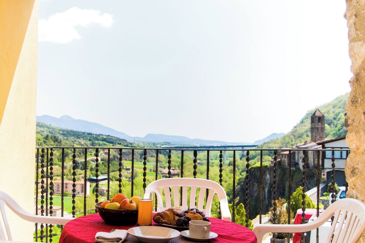 A balcony with a table set for breakfast, overlooking a mountainous landscape.