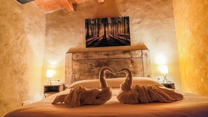 Una habitación acogedora con una cama, dos mesitas de noche, un cuadro de un bosque y un techo con vigas a la vista.