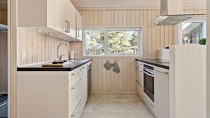 A compact kitchen with wooden paneling, a window with a view, and modern appliances. - Pet friendly home in ålbæk with WiFi (Ålbæk)