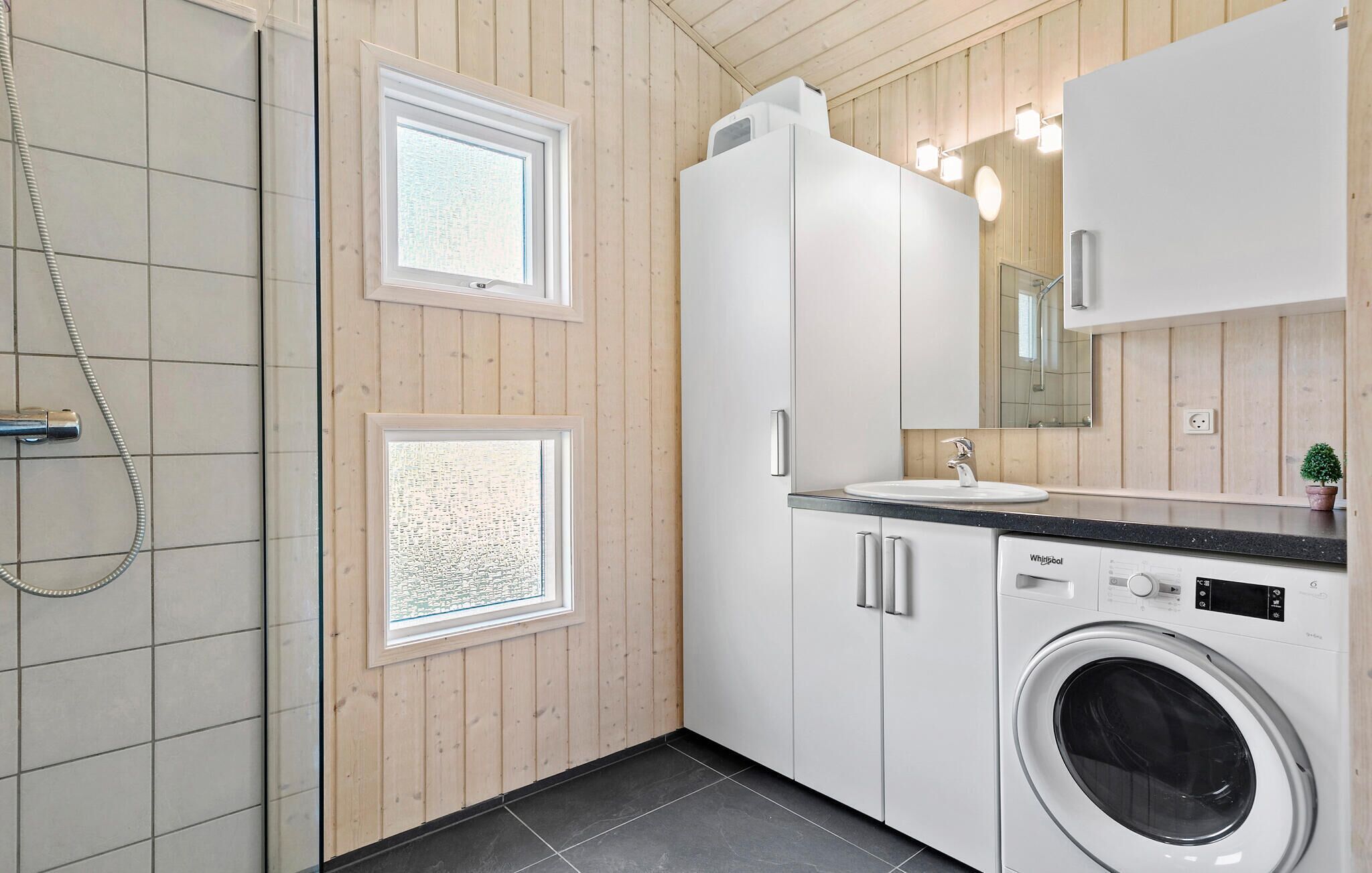 Une salle de bain moderne équipée d’une douche, d’un lavabo, d’un miroir et d’un lave-linge.
