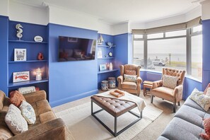 A living room with a large TV, blue walls, and a view of the sea.