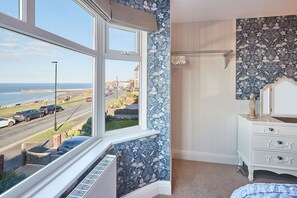 A bedroom with a bay window overlooking a street and a coastal view.