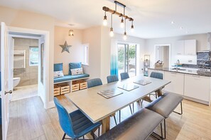 A modern kitchen with a large island, a dining area with a long table and chairs, and a seating area with a bench and cushions. - Sea View 5* Property, Sleeps 10, Parking, Dogs (Whitby)