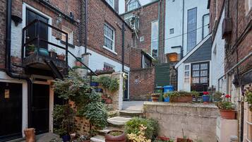 A narrow alleyway with brick buildings, a staircase, and various potted plants.