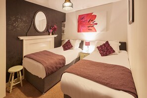 A double bed with a nightstand, a mirror, a floral wall, and a red abstract painting.