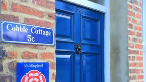 A blue door with a 'VisitEngland' sign and a 'Cobble Cottage 5c' sign on the wall.