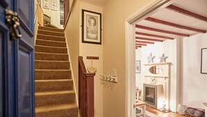 A staircase leading to a second floor, a coat rack with a sign, and a fireplace with decorative items.
