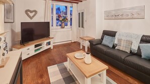 A living room with a TV, a sofa, a coffee table, and a window with flowers.