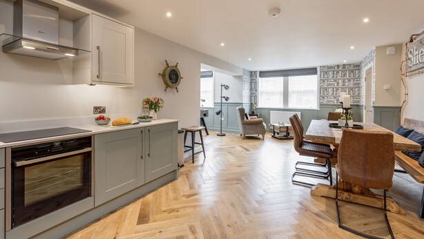 A modern kitchen with built-in appliances, a dining area with wooden flooring, and a view of the living room.