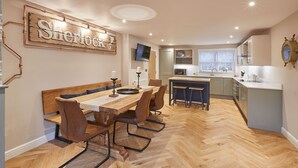 A dining area with a wooden table and chairs, a kitchen with a microwave, and a sign that reads 'Sherlock'.