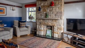 Ein Wohnzimmer mit Kamin aus Stein, einem Fernseher und einer Couch mit gemusterten Kissen.