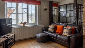 Ein Wohnzimmer mit einer Ledersofa, einem Fernseher auf einem Schrank, einem Fenster mit roter Vorhangschiene und einer Steinwand.