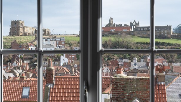 Blick durch ein Fenster auf eine Stadtlandschaft mit historischen Gebäuden und roten Ziegeldächern.
