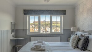 A bedroom with a large window, a bed with white linens, a bedside table with a lamp, and a view of the outside. - Elevated Dog friendly Cottage with Stunning Views (Whitby)