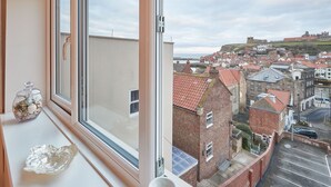 A room with a large window overlooking a historic town with red-roofed buildings and a prominent castle on a hill.