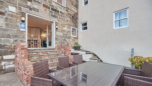 A stone building with a glass door entrance, wicker furniture, and a clear glass table.