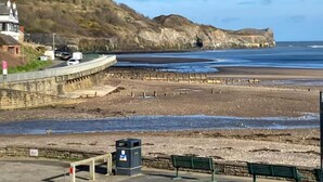 Une route côtière bordée d’une plage, d’un mur de pierres et d’un bâtiment doté d’une cheminée.