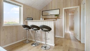 Una cocina moderna con paneles de madera, un ventanal con vistas, una barra con taburetes y un espejo sobre la encimera.