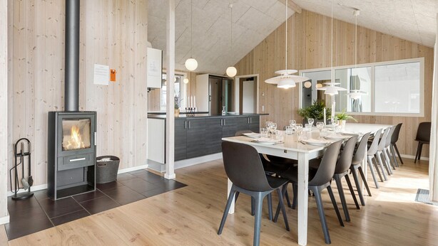Una cocina moderna con una isla central, un comedor con una mesa larga y sillas, y un estufa de leña.