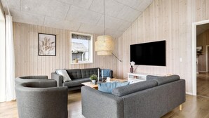 Una sala moderna con un sofá seccional gris, un sillón redondo gris, una mesa de centro y un televisor en la pared.