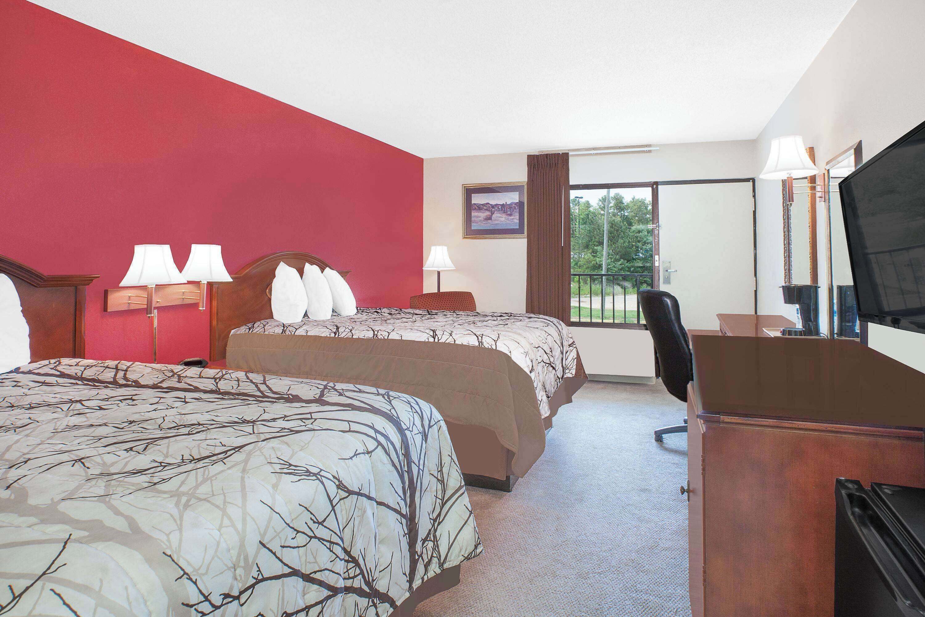 A hotel room with two beds, a desk, a chair, a TV, and a window with a view of trees.