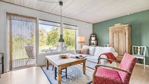 A spacious living room with a large window, a wooden table, a white sofa, and a red patterned chair. - 3 bedroom lovely home in Høng (Høng)