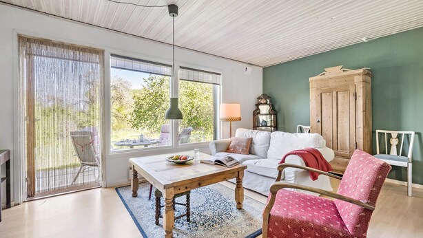 A spacious living room with a large window, a wooden table, a white sofa, and a red patterned chair. - 3 bedroom lovely home in Høng (Høng)