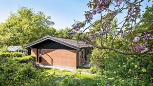 A small brick building with a sloped roof, surrounded by lush greenery and flowering trees. - 3 bedroom lovely home in Høng (Høng)