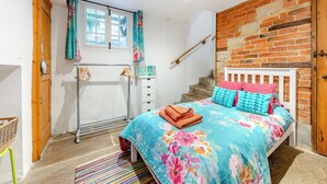 A bedroom with a brick wall, a bed with colorful bedding, a window with curtains, and a wooden door. - 4 bedroom accommodation in Stamford (Stamford)