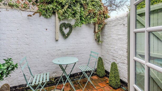 A small outdoor seating area with a white brick wall, a heart-shaped decoration, and a window. - 4 bedroom accommodation in Stamford (Stamford)