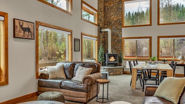 A cozy living room with a fireplace, leather furniture, and large windows offering a forest view. - Cozy Chinook Cabin (Naches)