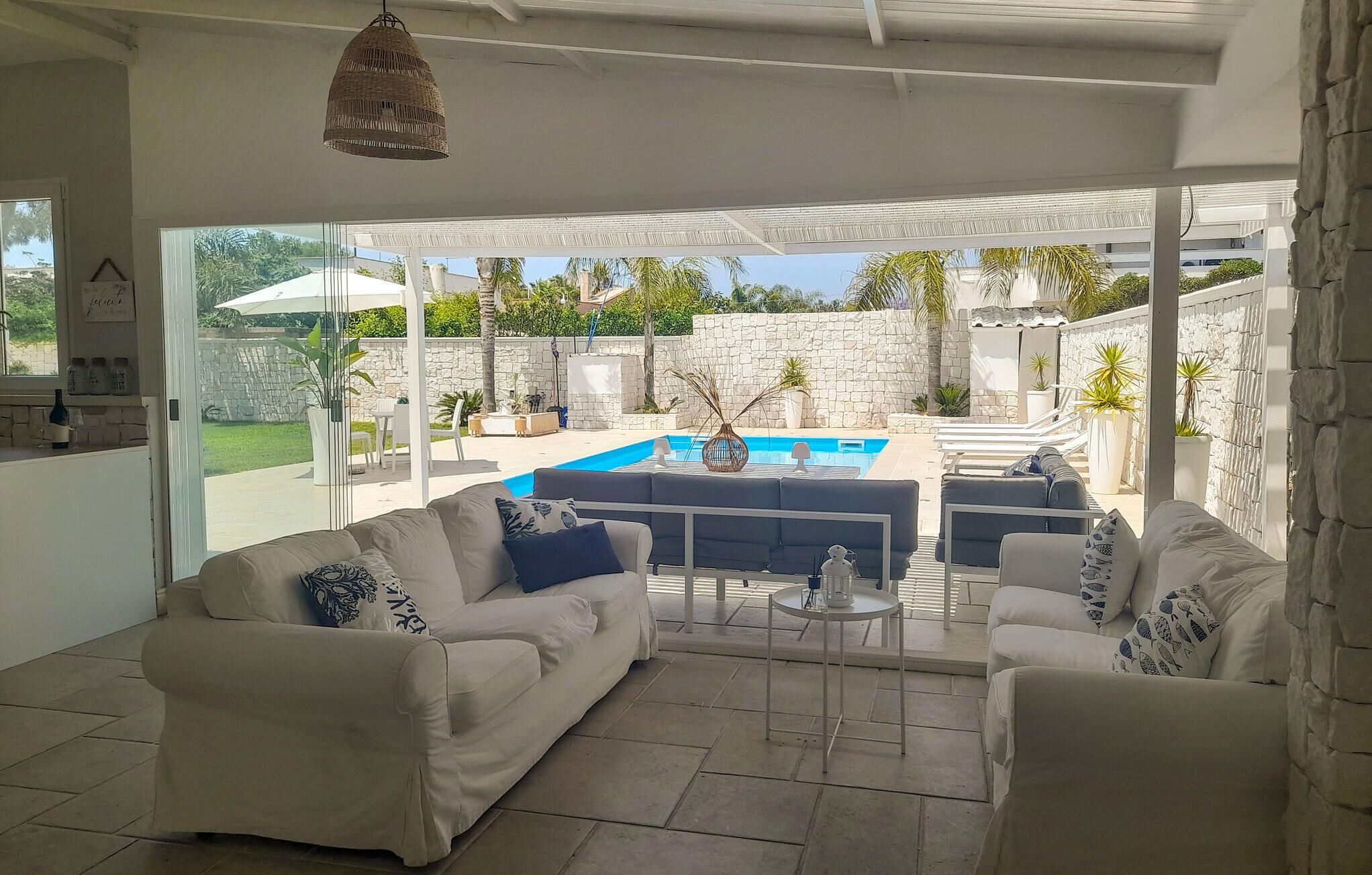 A spacious living area with a white sofa, a coffee table, and a view of a swimming pool and garden.