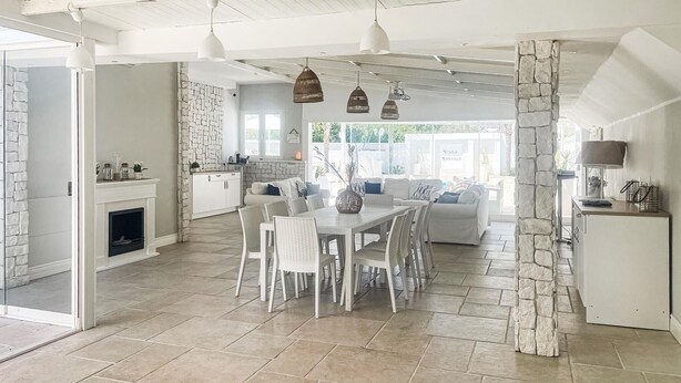 A spacious living area with a dining table, white wicker furniture, stone accents, and a stone pillar.