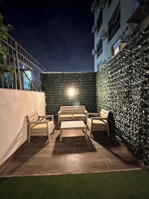 Ein Patio mit Sitzgelegenheit, eine mit Pflanzen bewachsene Wand und ein Gebäude im Hintergrund.
