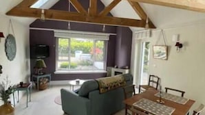 A spacious living area with a high ceiling, wooden beams, a sofa, a dining table, and a television.