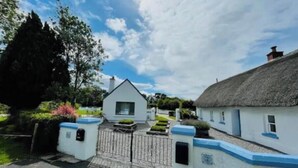 A traditional white cottage with a thatched roof, a gated entrance, and a well-maintained garden.