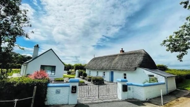 A traditional white house with a thatched roof, a gated entrance, and a well-maintained garden.