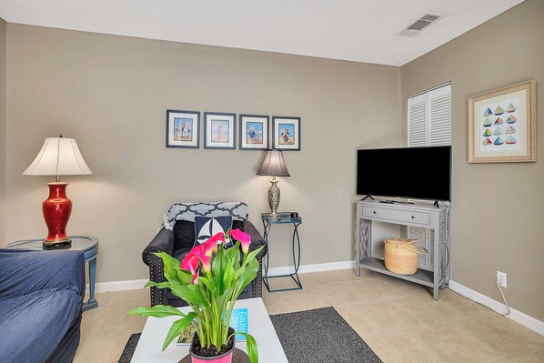A living room with a sofa, a coffee table with a plant, a TV, and framed artwork on the wall.