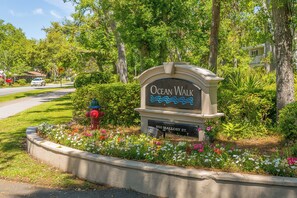 A sign for Ocean Walk at 850 Mallory St., surrounded by a landscaped garden with flowers and trees. - Island Oasis: Your poolside escape! (St. Simons Island)