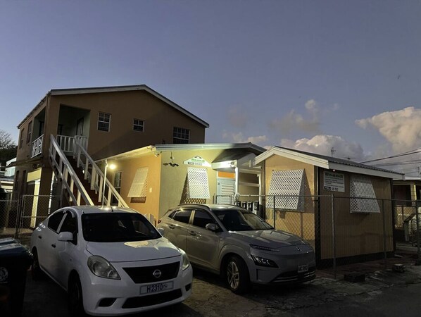 Um edifício com escadaria que dá para um segundo andar, entrada coberta e dois carros estacionados.