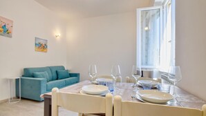 Uma área de refeições com mesa posta para quatro pessoas, um sofá azul e uma janela com cortinas.