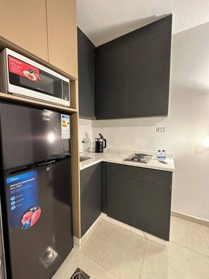 A compact kitchen with a black refrigerator, a microwave, and a coffee maker on the counter. - Stylish Luxe Apartment (Amman)