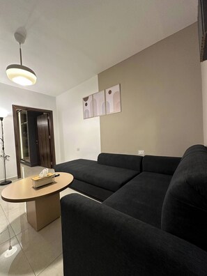 A modern living room with a sectional sofa, a round coffee table, and a ceiling light fixture. - Stylish Luxe Apartment (Amman)
