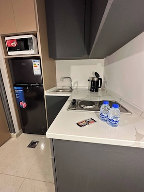 Een kleine keuken met een magnetron, koelkast, spoelbak en koffiezetapparaat.
